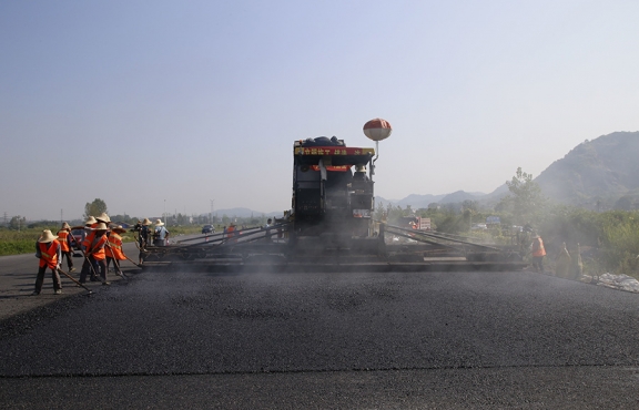 2019年8月，宜春經(jīng)開(kāi)區(qū)S311路面攤鋪現(xiàn)場(chǎng)，工友們輔助路面兩側(cè)的分料、補(bǔ)窩等作業(yè)